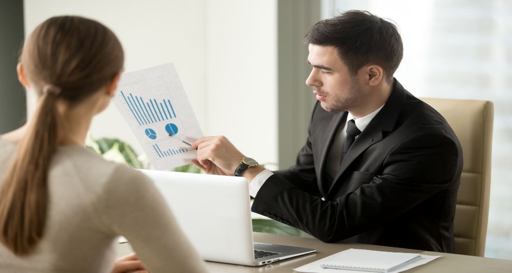 Imagen de un hombre mostrando gráficos a una mujer en una reunión de negocios, usada en una entrada del blog de Chapa Cambio sobre cómo empezar a invertir tus ahorros en dólares
