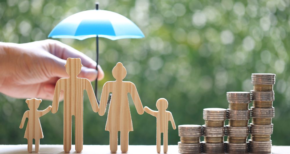Piezas de madera representando una familia bajo un paraguas protector con monedas apiladas en una entrada en el blog de Chapa Cambio sobre estrategias de ahorro familiar