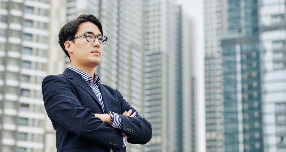 Foto de un hombre de negocios con los brazos cruzados frente a edificios altos, usada en una entrada en el blog de Chapa Cambio sobre las diferencias entre un emprendedor y un inversionista y sus roles en el mercado financiero