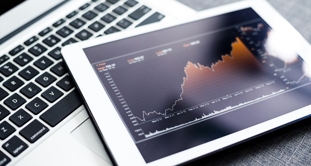Pieza gráfica utilizada en la entrada de Chapa Cambio sobre fondos indexados, mostrando un gráfico de rendimiento en una tablet sobre una laptop, ilustrando el seguimiento de los índices bursátiles